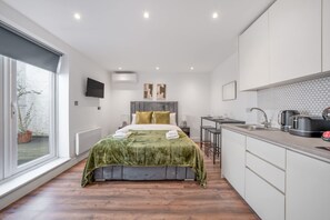 Ein modernes Schlafzimmer mit einem großen Bett, einer kleinen Küchenzeile und Blick ins Freie.