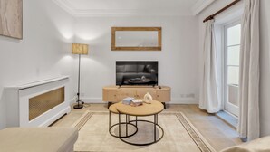 A modern living room with a fireplace, a television, a round coffee table, and a large window with curtains. - Modern Split-level Apartment in Knightsbridge (London)
