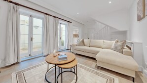 A living room with a beige sofa, a round wooden coffee table, and a large window with curtains. - Modern Split-level Apartment in Knightsbridge (London)
