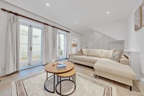 A living room with a beige sofa, a round wooden coffee table, and a large window with curtains. - Modern Split-level Apartment in Knightsbridge (London)