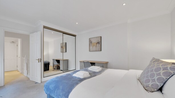 A bedroom with a bed, a desk, a chair, a mirror, and a door leading to another room. - Modern Split-level Apartment in Knightsbridge (London)
