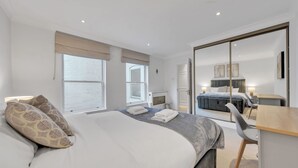 A modern hotel room with a large bed, a desk, a chair, and a sliding door leading to a balcony. - Modern Split-level Apartment in Knightsbridge (London)