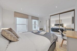 A modern hotel room with a large bed, a desk, a chair, and a sliding door leading to a balcony. - Modern Split-level Apartment in Knightsbridge (London)