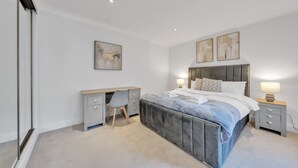 A bedroom with a large bed, a desk, and two bedside tables with lamps. - Modern Split-level Apartment in Knightsbridge (London)