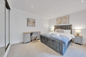 A bedroom with a large bed, a desk, and two bedside tables with lamps. - Modern Split-level Apartment in Knightsbridge (London)