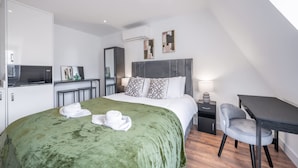 A modern hotel room with a large bed, a desk, a chair, a TV, and a wardrobe. - Top Floor Studio With View in Knightsbridge (London)