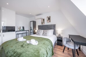 A modern hotel room with a large bed, a desk, a chair, a TV, and a wardrobe. - Top Floor Studio With View in Knightsbridge (London)