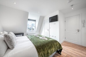 A modern bedroom with a bed, a TV mounted on the wall, and a window with a view of buildings. - Top Floor Studio With View in Knightsbridge (London)