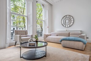 A modern living room with a round glass coffee table, two sofas, and large windows offering a city view. - Spacious Knightsbridge Apartment With Balcony (London)