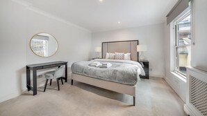 Quarto com cama, mesa de cabeceira, abajur, escrivaninha, cadeira e janela.