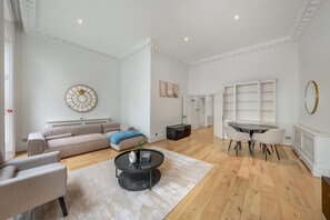 A spacious living room with a sofa, coffee table, and a dining area with chairs and a table. - Spacious Knightsbridge Apartment With Balcony (London)