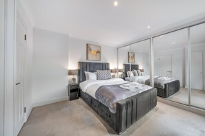A modern bedroom with a large bed, bedside tables, a mirror, and a wardrobe. - Spacious Knightsbridge Apartment With Balcony (London)