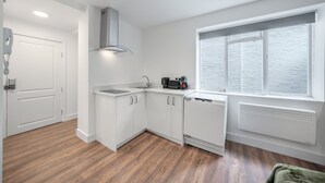 A modern kitchen with white cabinetry, a built-in dishwasher, and a window with a view. - Superior Ground Floor Studio in Knightsbridge (London)