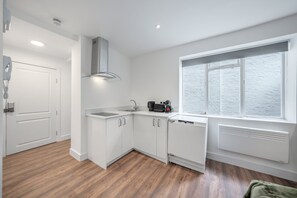 A modern kitchen with white cabinetry, a built-in dishwasher, and a window with a view. - Superior Ground Floor Studio in Knightsbridge (London)