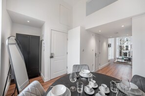 Uma sala de jantar com mesa posta para quatro, um sofá preto e vista para uma varanda.