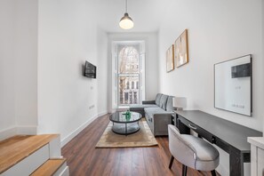 Uma sala moderna com uma mesa de centro redonda de vidro, sofá cinza e uma área de jantar com bancada escura.