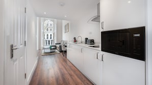 A modern kitchen with white cabinetry, a built-in microwave, and a coffee maker. - Deluxe Studio Mezzanine With Balcony in Knightsbridge (London)