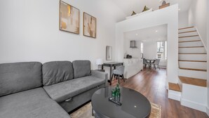 A modern living room with a grey sofa, a round coffee table, and a staircase leading to an upper level. - Deluxe Studio Mezzanine With Balcony in Knightsbridge (London)