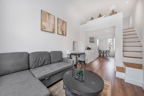 Uma sala de estar moderna com um sofá cinzento, uma mesa de centro redonda e uma escada que dá para um andar superior.