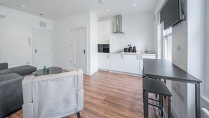 A modern kitchen with white cabinets, a stainless steel range hood, and a flat-screen TV mounted on the wall. - Charming One Bedroom Flat in Knightsbridge (London)