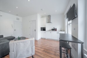 A modern kitchen with white cabinets, a stainless steel range hood, and a flat-screen TV mounted on the wall. - Charming One Bedroom Flat in Knightsbridge (London)