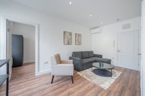 A modern living room with a grey sectional sofa, a beige armchair, and a coffee table. - Charming One Bedroom Flat in Knightsbridge (London)