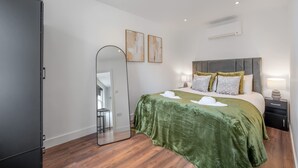 A modern bedroom with a large bed, a mirror, two wall art pieces, a nightstand, and a wardrobe. - Top Floor One-bed With View in Knightsbridge (London)