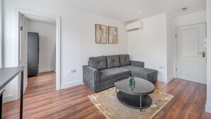 A modern living room with a grey sectional sofa, a round coffee table, and a beige rug. - Top Floor One-bed With View in Knightsbridge (London)