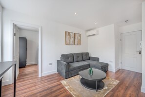 A modern living room with a grey sectional sofa, a round coffee table, and a beige rug. - Top Floor One-bed With View in Knightsbridge (London)