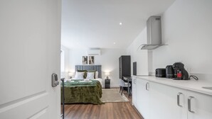 A modern hotel room with a bed, a desk, a television, and a kitchenette. - Modern Studio in Knightsbridge (London)
