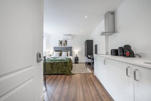 A modern hotel room with a bed, a desk, a television, and a kitchenette. - Modern Studio in Knightsbridge (London)