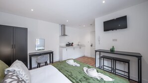 A modern hotel room with a bed, a desk, a TV, and a kitchenette. - Modern Studio in Knightsbridge (London)