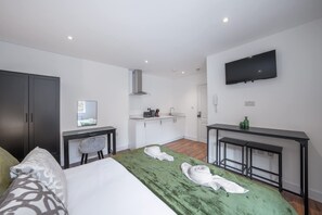 A modern hotel room with a bed, a desk, a TV, and a kitchenette. - Modern Studio in Knightsbridge (London)