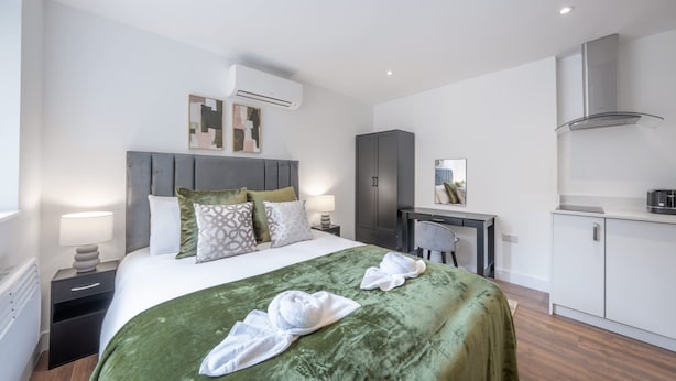 A modern hotel room with a bed, a desk, a wardrobe, and an air conditioning unit. - Modern Studio in Knightsbridge (London)