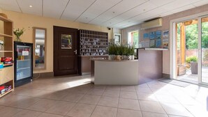 A reception area with a tiled floor, a reception desk, a wall-mounted wine cooler, and a door leading to another room. - Séjour montagne près du domaine skiable | Piscine (Ax-Les-Thermes)