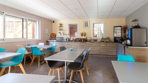 A dining area with tables and chairs, a kitchen area with appliances, and a view of the outside. - Séjour montagne près du domaine skiable | Piscine (Ax-Les-Thermes)