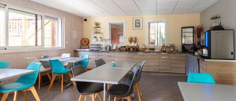 A dining area with tables and chairs, a kitchen area with appliances, and a view of the outside.