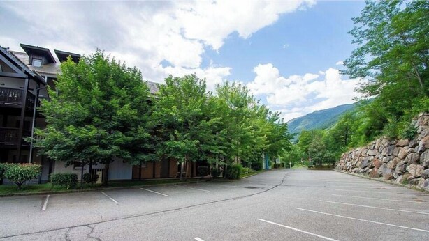 A parking lot with a building on the left and a mountain in the background. - Séjour montagne près du domaine skiable | Piscine (Ax-Les-Thermes)