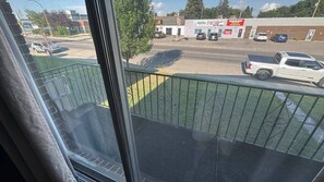 Uitzicht vanuit een raam op een parkeerplaats met een groene hekken, een gebouw met de tekst 'Ability Physiotherapy & Wellness', en verschillende geparkeerde auto's.