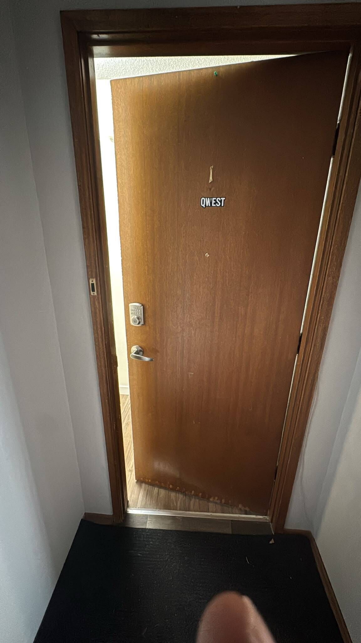 Une porte en bois avec une plaque portant l’inscription « QWEST », un trou de serrure et une poignée de porte.
