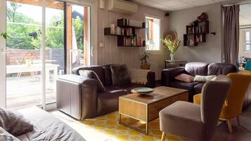 Een woonkamer met een bank, fauteuil en salontafel. Er staan boekenkasten en een raam met uitzicht op groen.