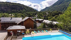 A swimming pool with lounge chairs, a wooden building, and a mountainous backdrop.