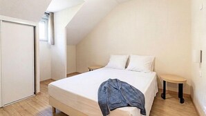 A bedroom with a sloped ceiling, a bed with white linens, a bedside table, and a small stool.