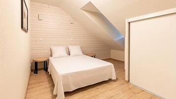 Een slaapkamer met een schuine kap, een bed met witte beddengoed, twee nachtkastjes en een houten vloer.
