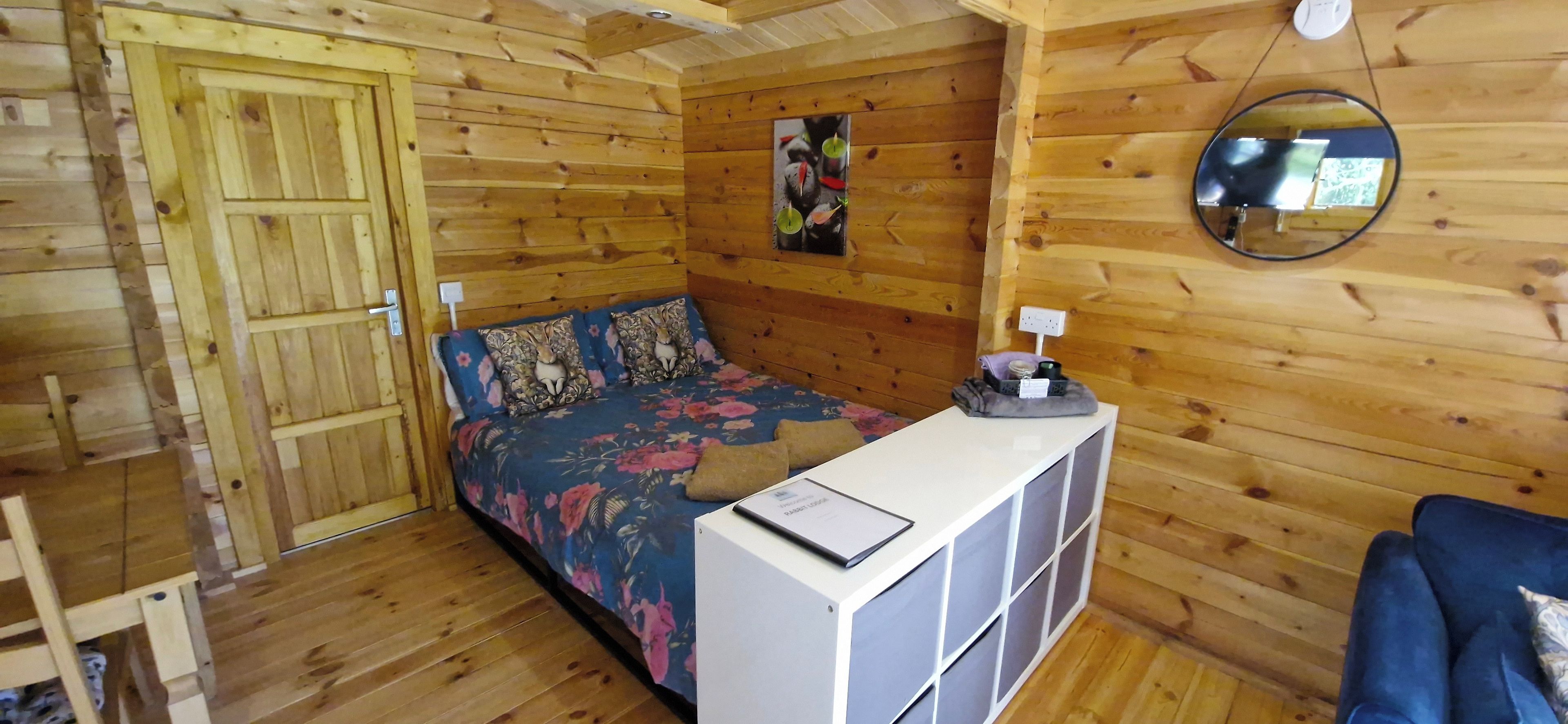 Una habitación tipo cabaña de madera con una cama, un escritorio pequeño y un espejo.