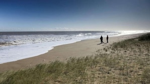 A beach with two people walking along the shore, waves crashing onto the sand, and a clear sky. - Rabbit Lodge Dog Friendly nr Anderby Creek (Alford)