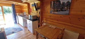 Interior de uma cabana de madeira com cozinha, sala de jantar e um quadro na parede.