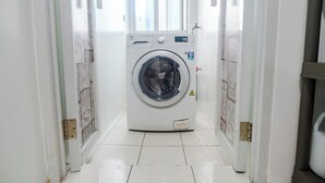 A front-loading washing machine in a narrow hallway with tiled flooring and white walls. - City Comfort at Seibu Tower (Taguig City)