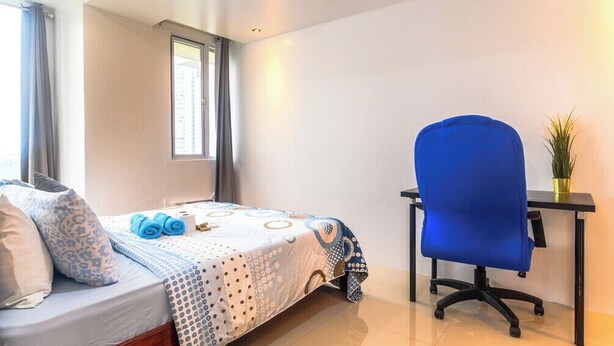 A bedroom with a bed, a blue chair, a small table with a plant, and a window. - City Comfort at Seibu Tower (Taguig City)