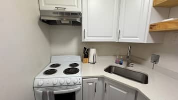 Une cuisine de taille réduite avec des meubles blancs, une cuisinière, un évier et une étagère en bois.